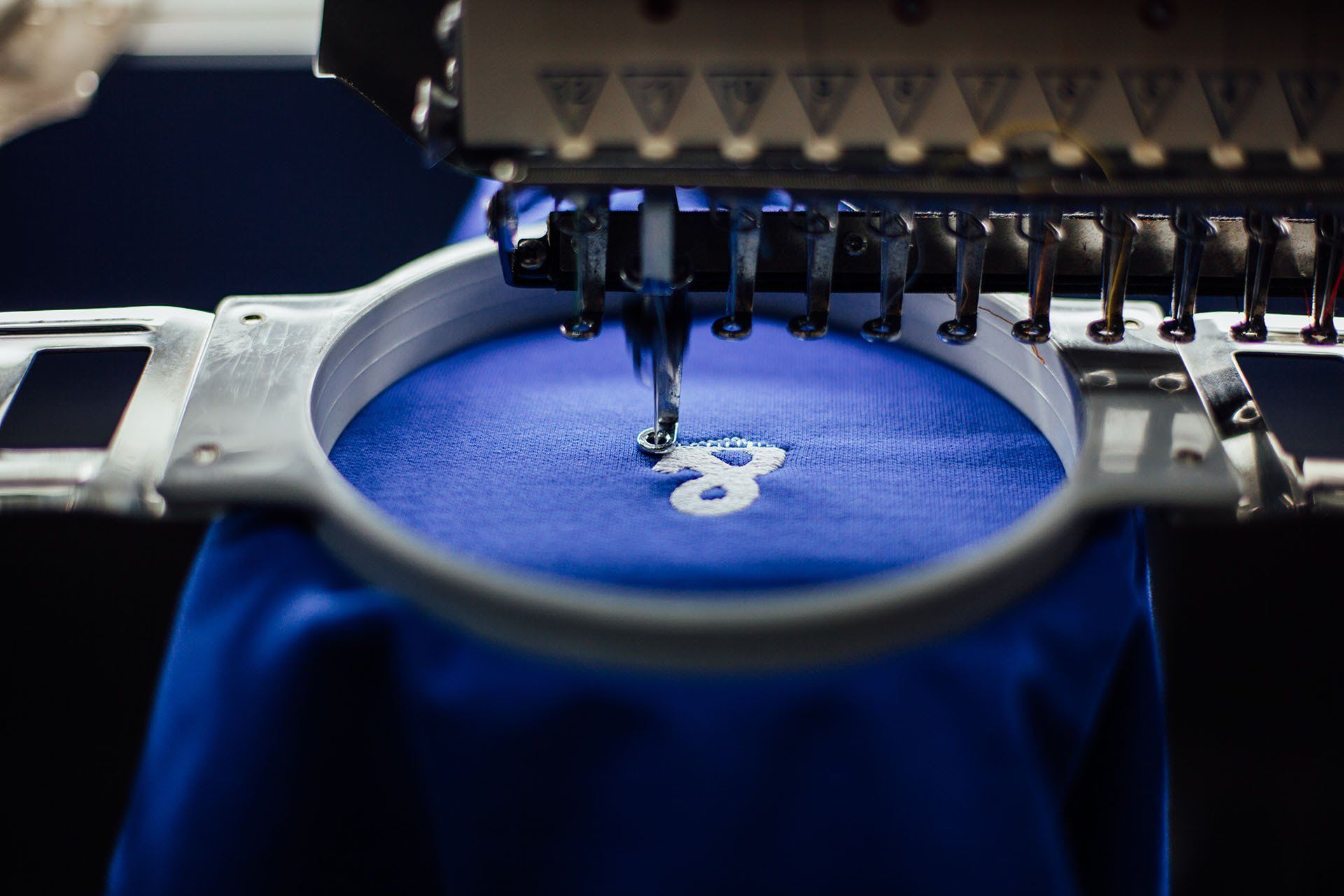 A machine is embroidery the number 8 on a blue shirt.
