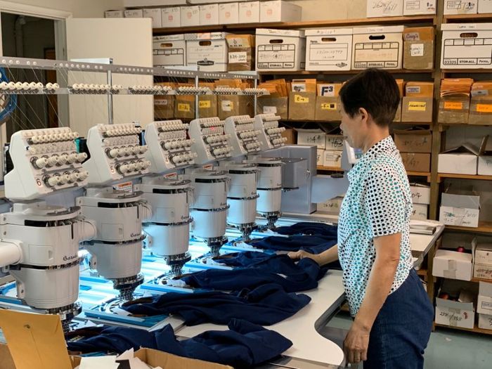 A woman is standing in front of a row of embroidery machines.