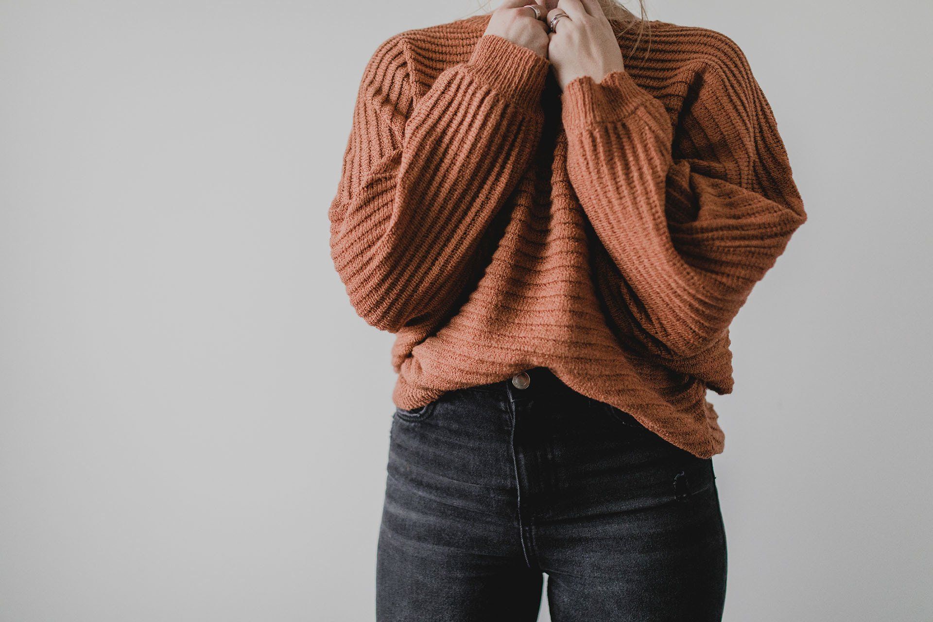 A woman is wearing an orange sweater and black jeans.