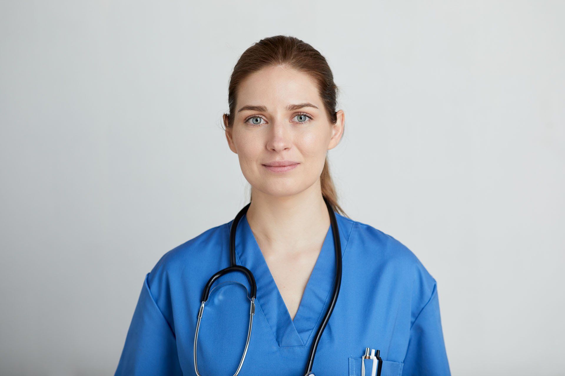 A female doctor is wearing a blue scrub and a stethoscope around her neck.