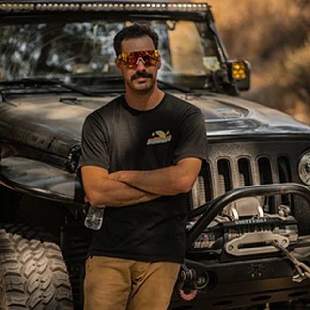 Man standing with arms crossed in front of a black off-road vehicle with large tires and a winch.