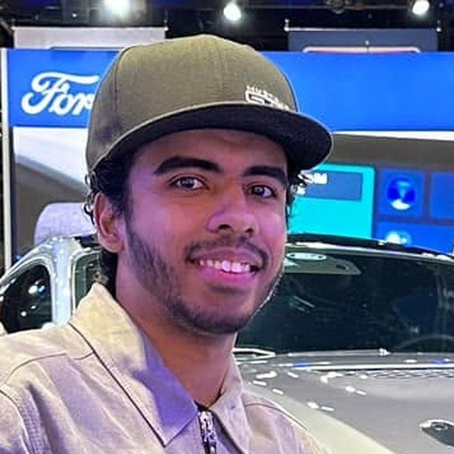 Smiling person in a gray cap posing at a Ford car display booth.