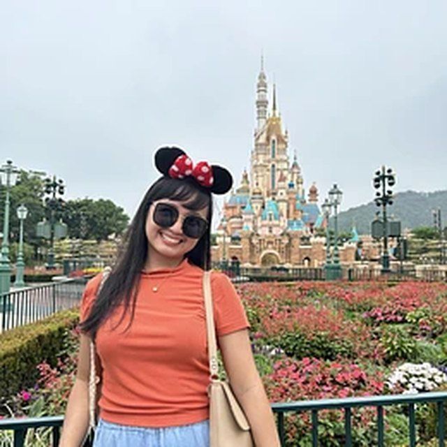 Woman in Minnie Mouse ears posing in front of a fairy-tale castle and flower garden at a theme park