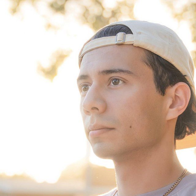 Man wearing a backward beige cap, looking to the side in warm sunset light