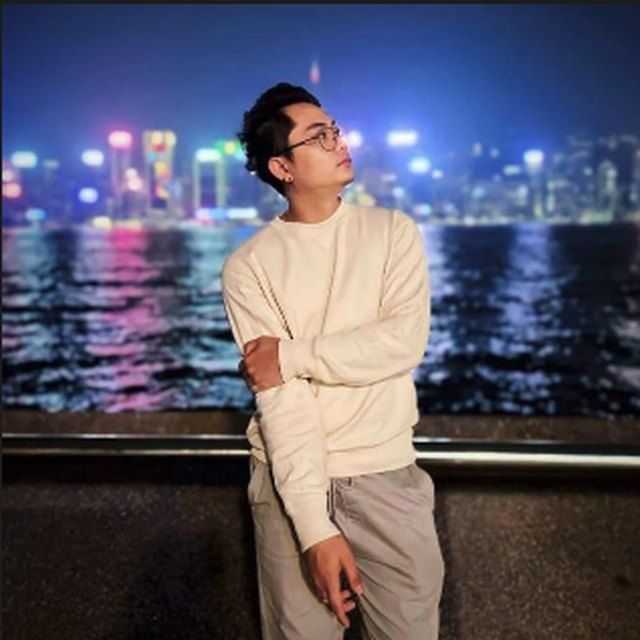 Person in a cream sweater posing by a waterfront at night with city lights in the background