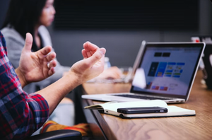 Hands gesturing during a meeting beside a laptop and notebook on a conference table