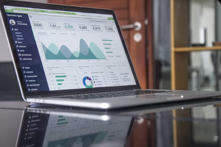 Laptop showing a business analytics dashboard with charts on a glass desk