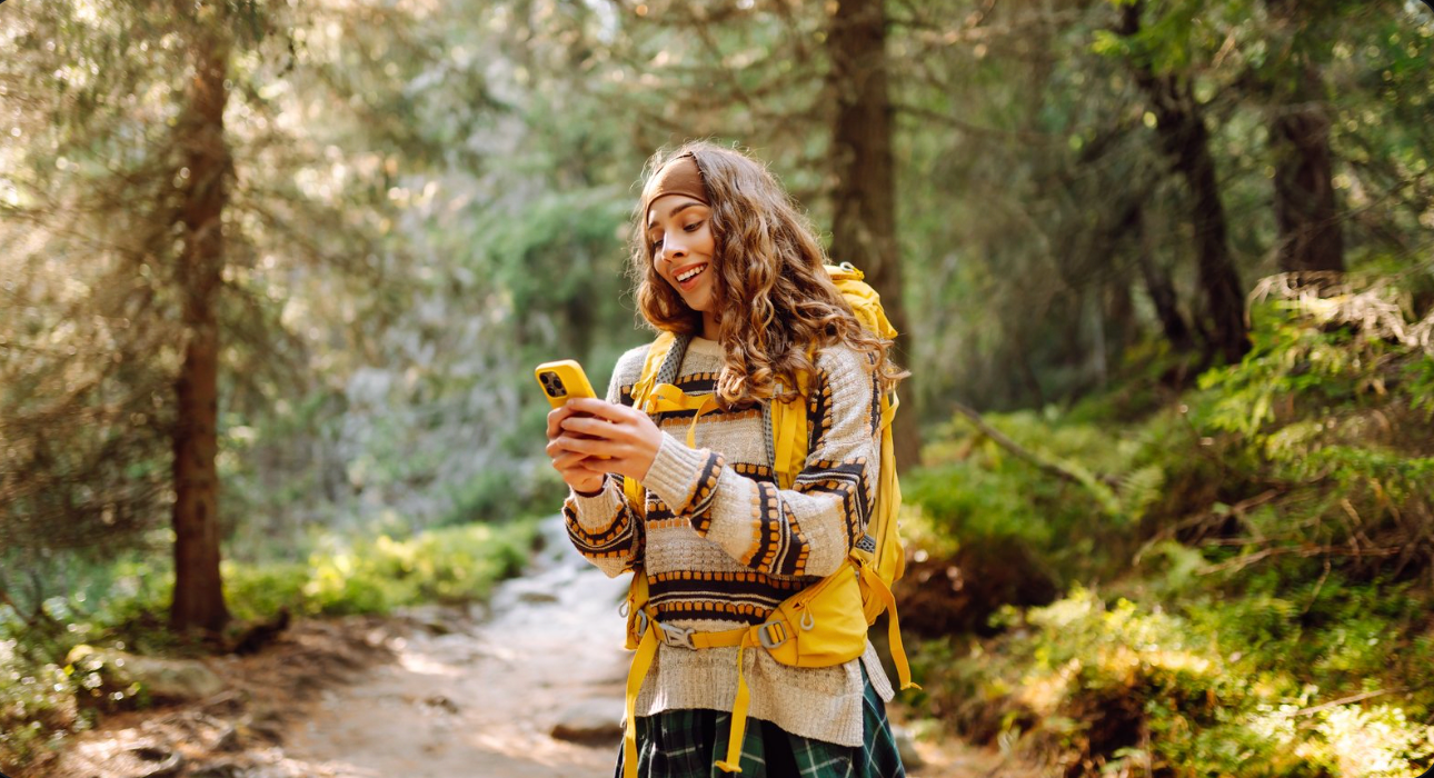 Person with a yellow backpack reading a phone on a forest trail