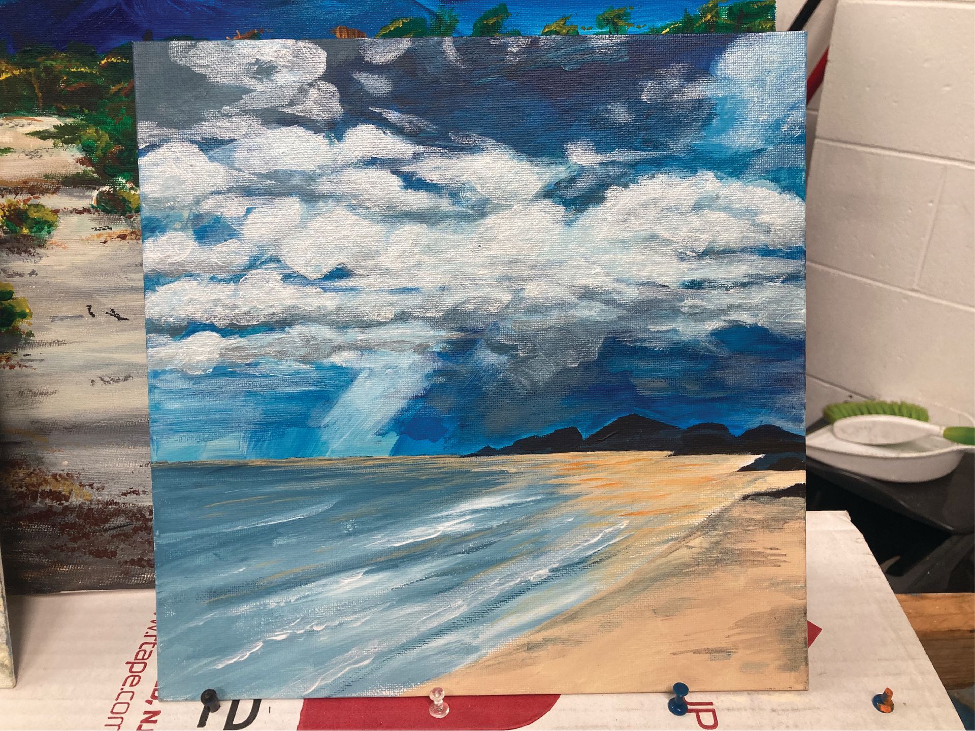 A painting of a beach with waves and clouds is sitting on a table — Cairns Custom T-Shirts In Cairns City, QLD