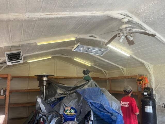 Two people in a tarp-covered workshop or garage working beneath a sloped ceiling with lights and equipment.
