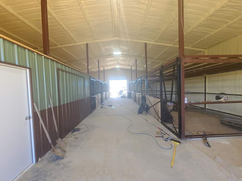 Long barn aisle with metal stalls, concrete floor, and bright daylight at the far end