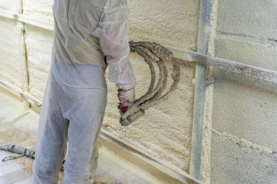 Worker spraying insulation onto a cinder block wall with a hose and nozzle