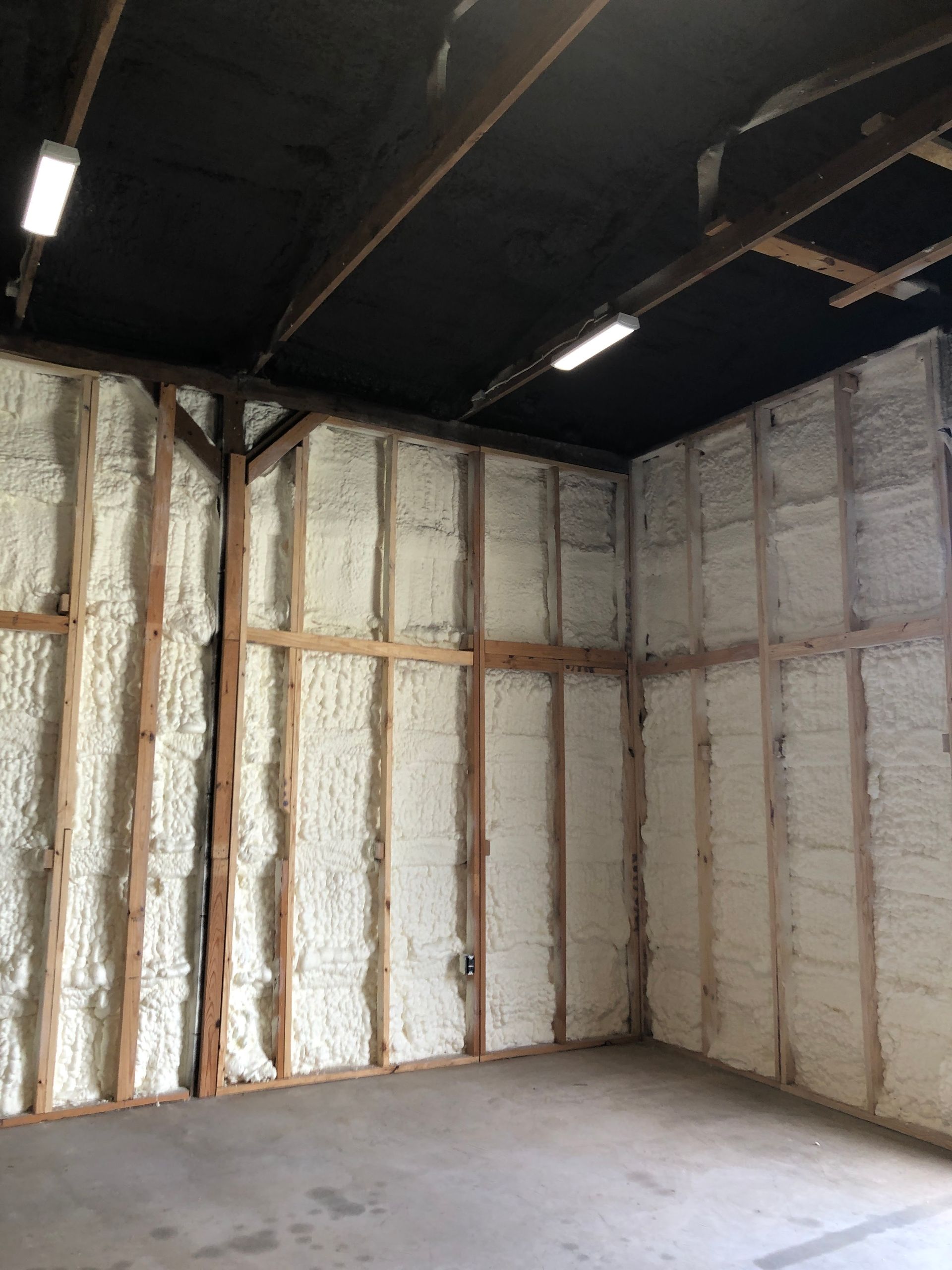 Empty insulated room with exposed spray foam walls and dark ceiling beams