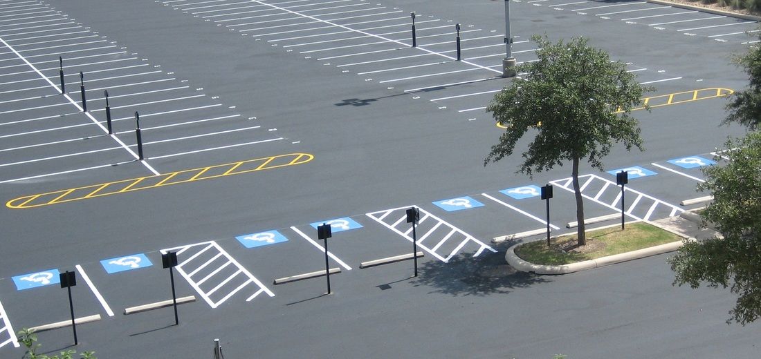 An aerial view of a mostly empty parking lot with clearly marked accessible parking spaces painted with blue symbols.
