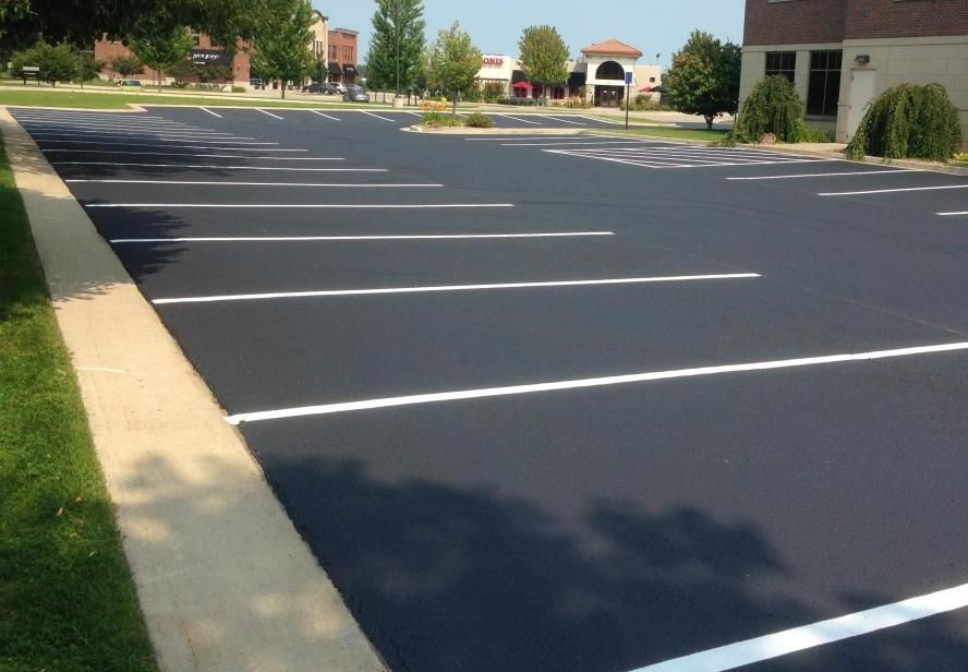 A freshly paved, empty parking lot with bright white painted parking space lines, bordered by a concrete curb and lawn.