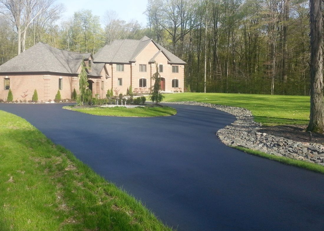 A large, multi-story brick house with a sprawling, freshly paved asphalt driveway leading to the entrance.
