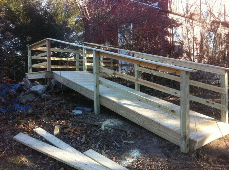 Wooden ramp with handrails providing accessibility to a building in a wooded area.