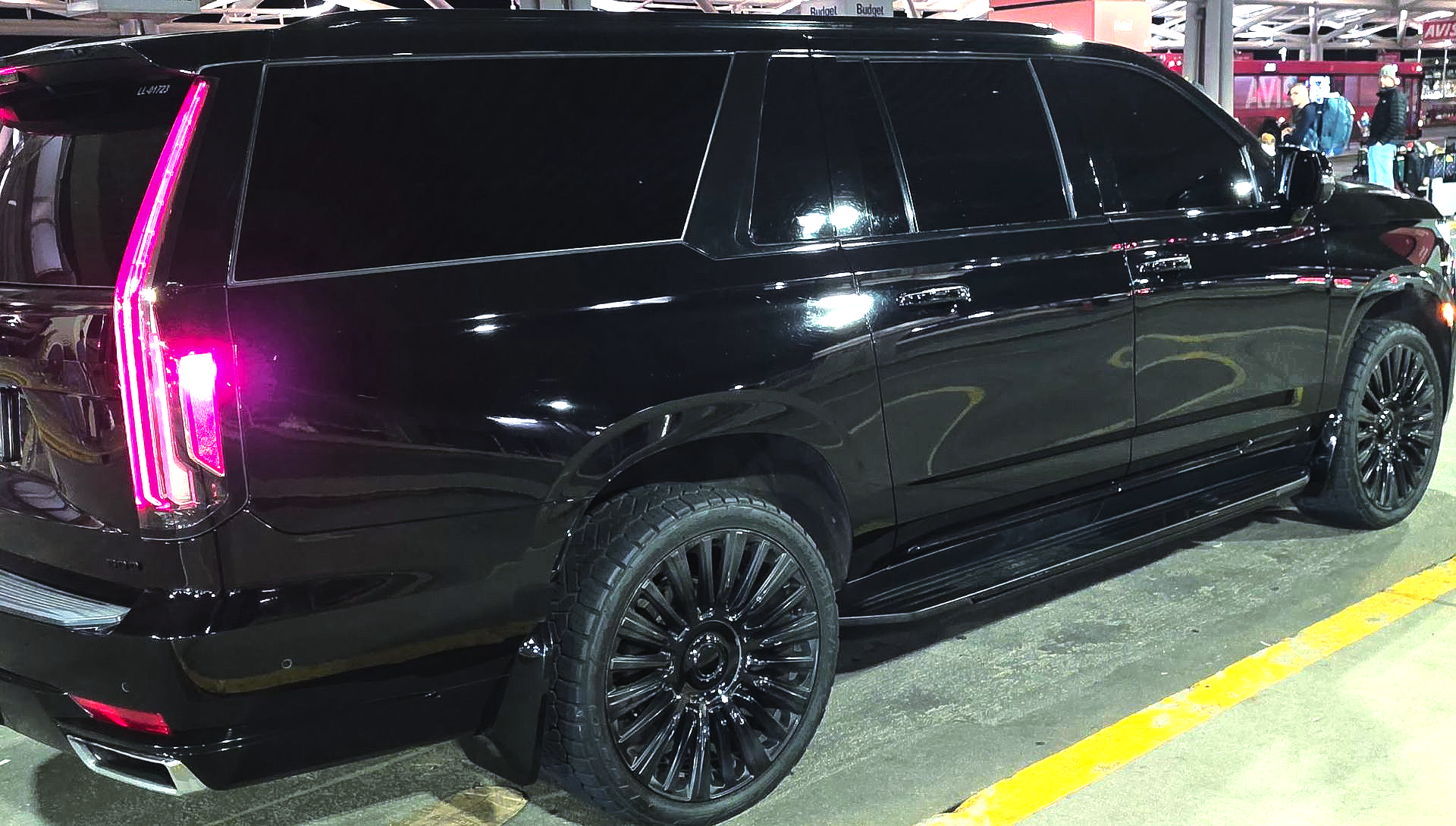 Black SUV with tinted windows and pink taillights parked in a lot at night