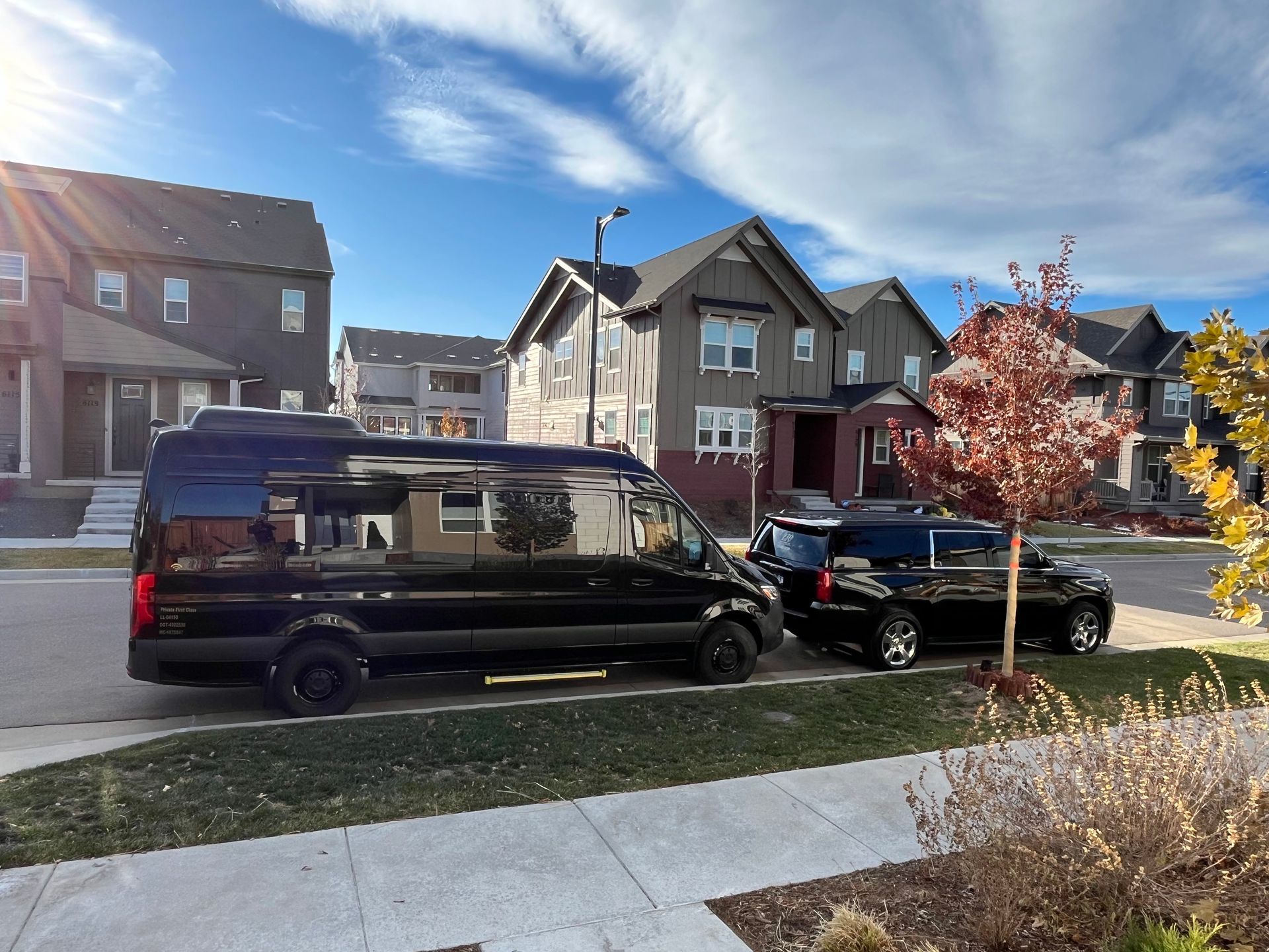 Black van and pickup parked on a sunny residential street with houses and autumn trees.