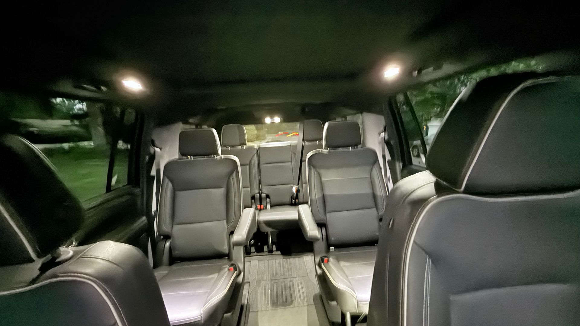 Interior of a black luxury van with gray leather seats and overhead lights, viewed from the front to rear.