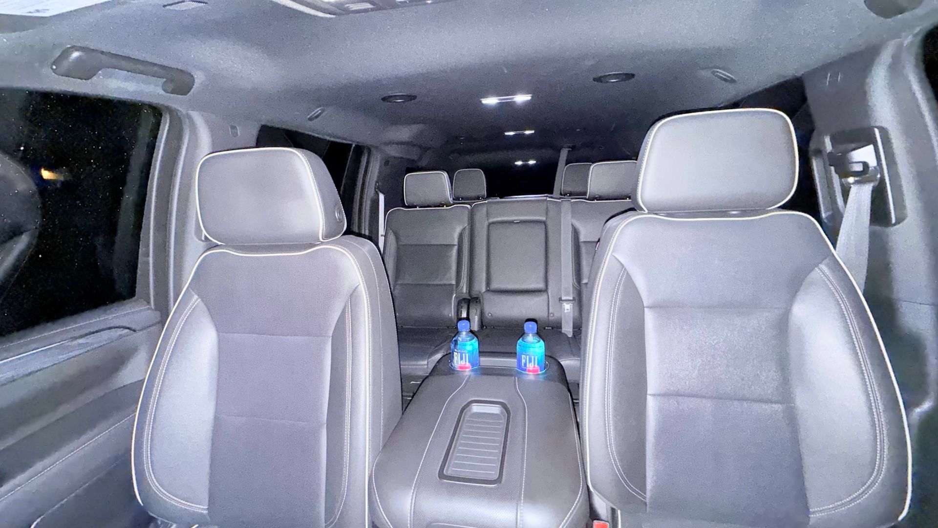 Interior of a gray minivan with three rows of empty seats and water bottles on the center console