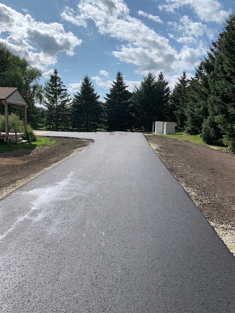 Trinity Asphalt Paving technician applying seal coating to a residential driveway in Iowa.