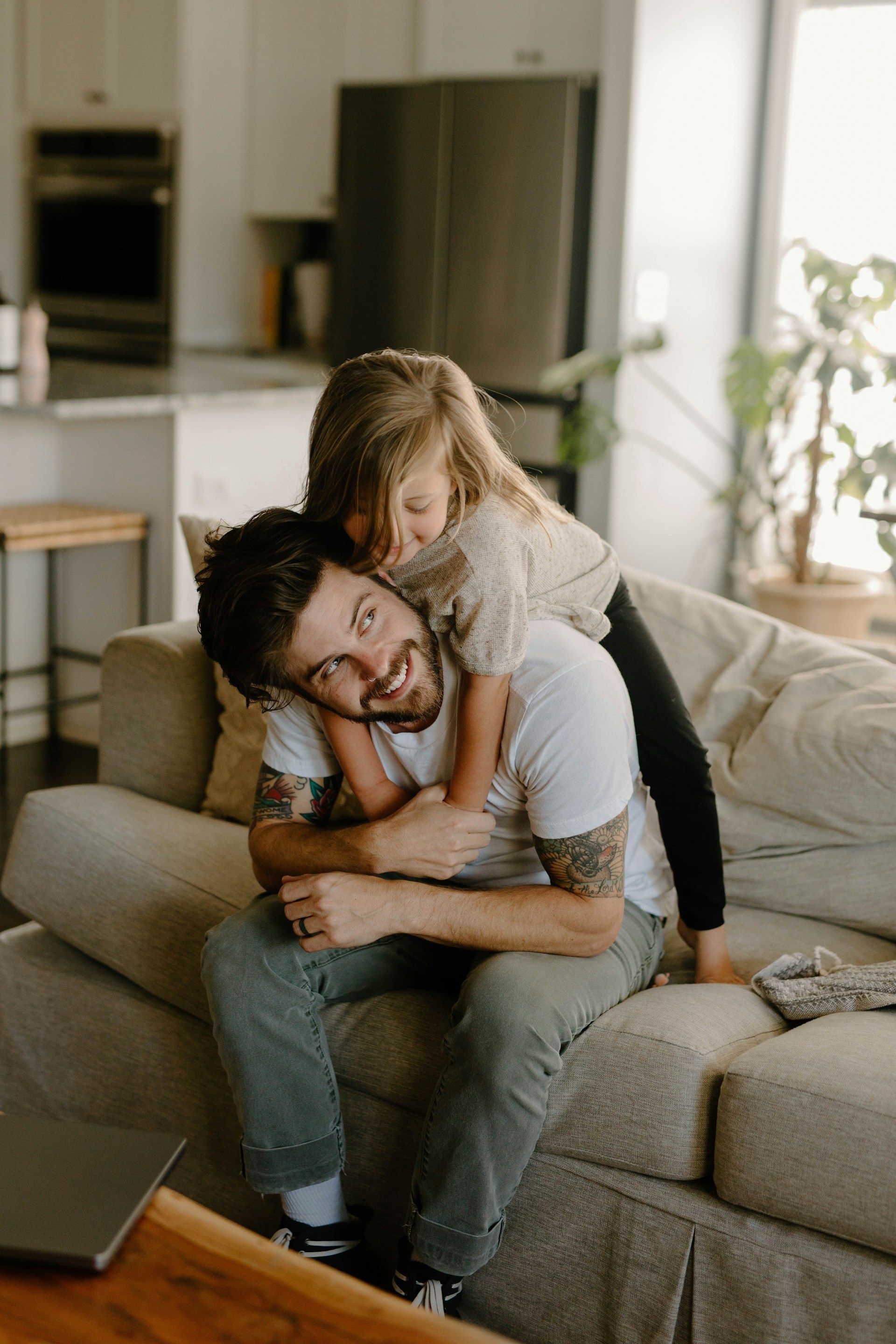 Couple hugging on a couch in a bright living room, with a laptop nearby.