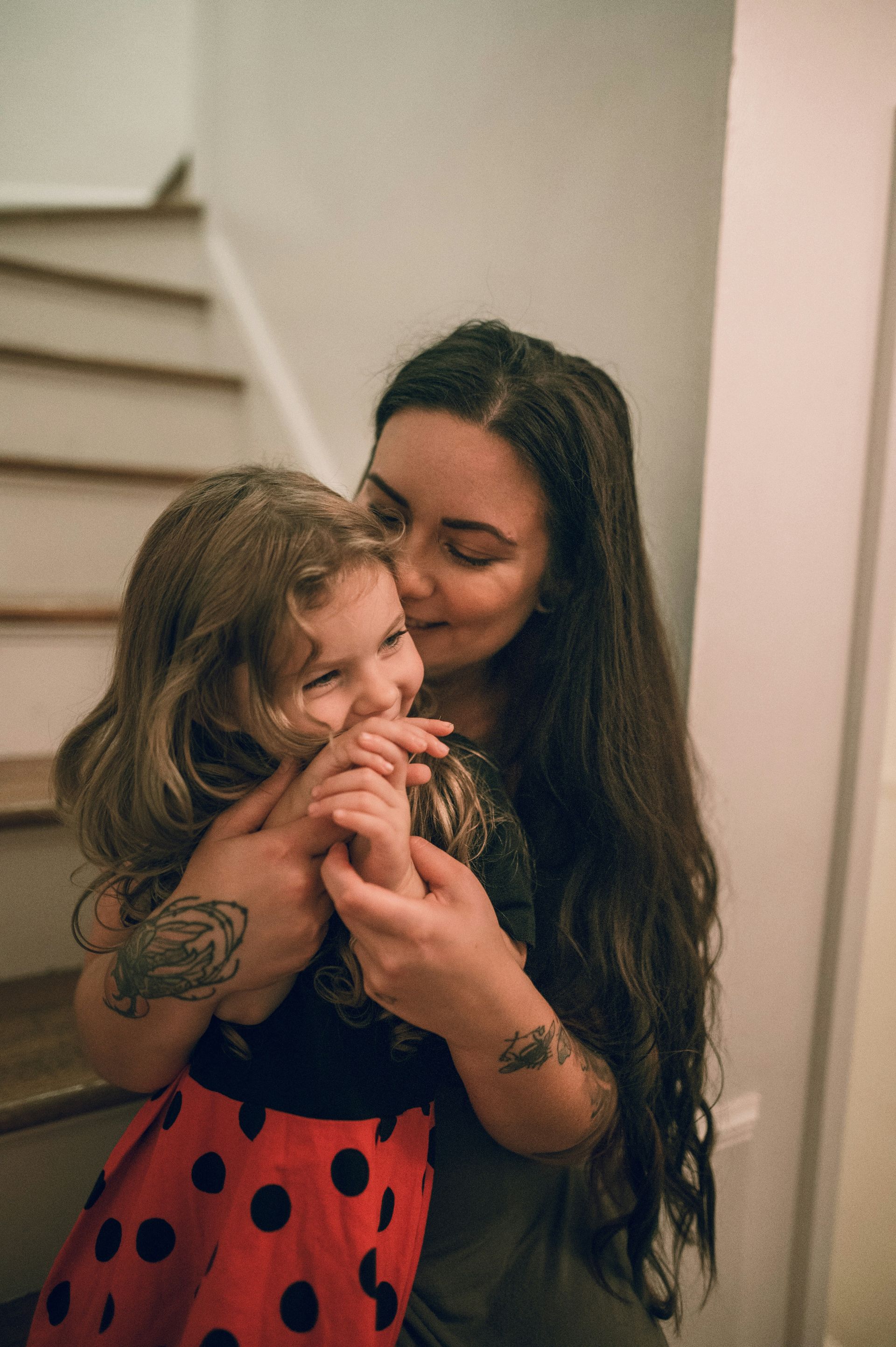 Woman with long dark hair cuddling a child in a red polka-dot dress indoors