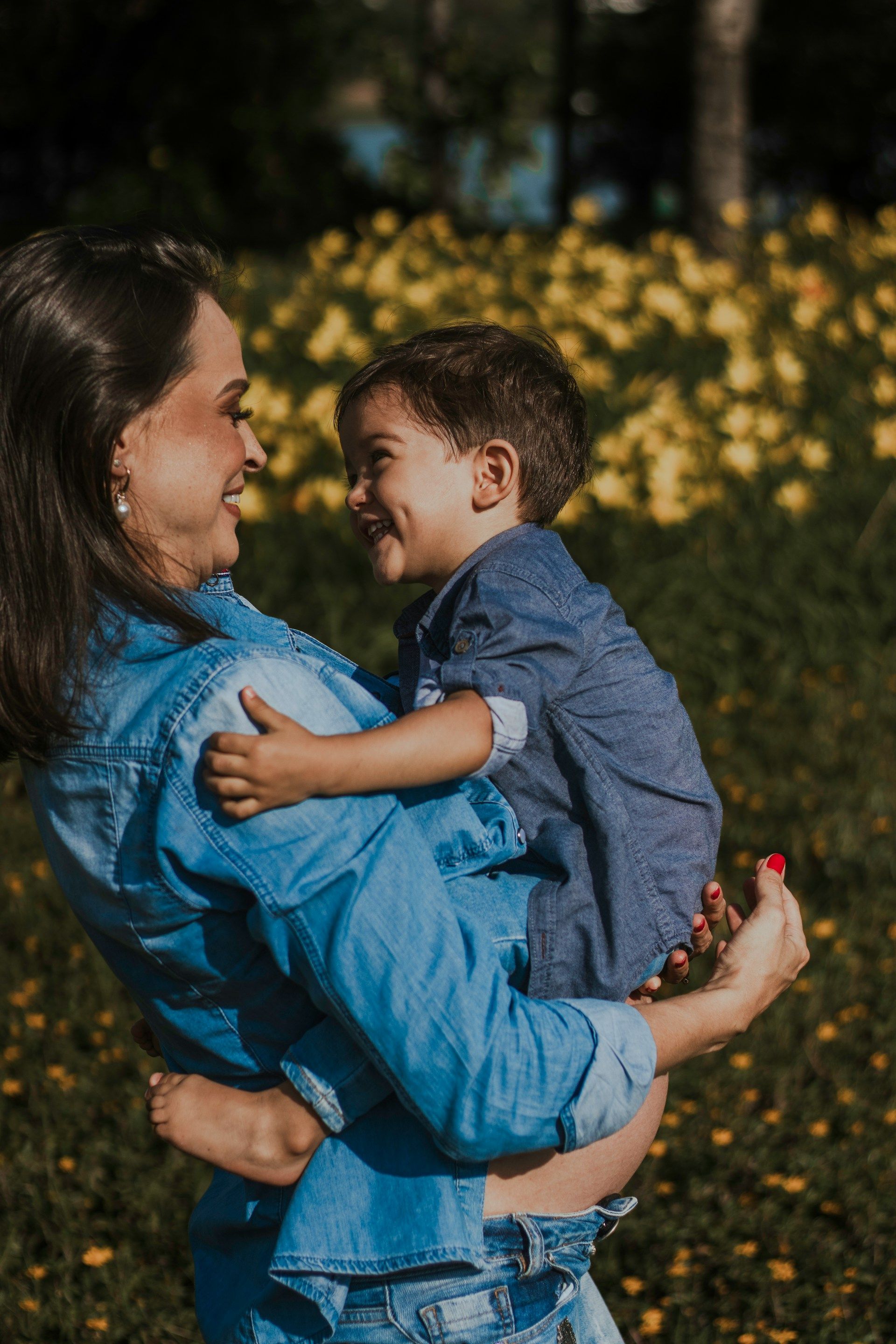 Woman in a blue shirt holding a smiling child in a flower-filled field.