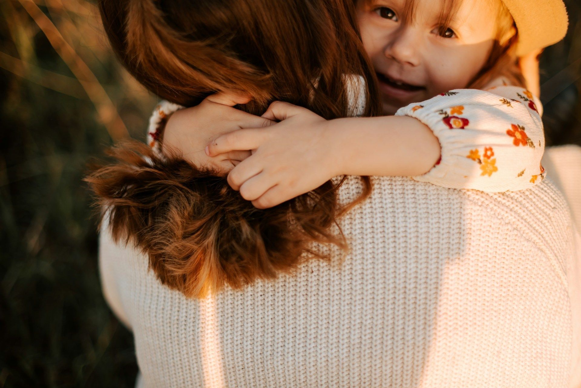 Child hugging an adult from behind in warm sunlight, with a close-up view of their embrace