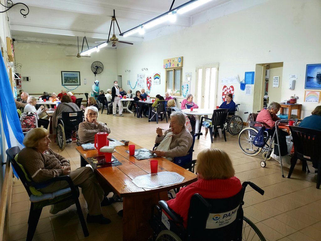 Personas sentadas en mesas en un luminoso salón comunitario, charlando durante una reunión.