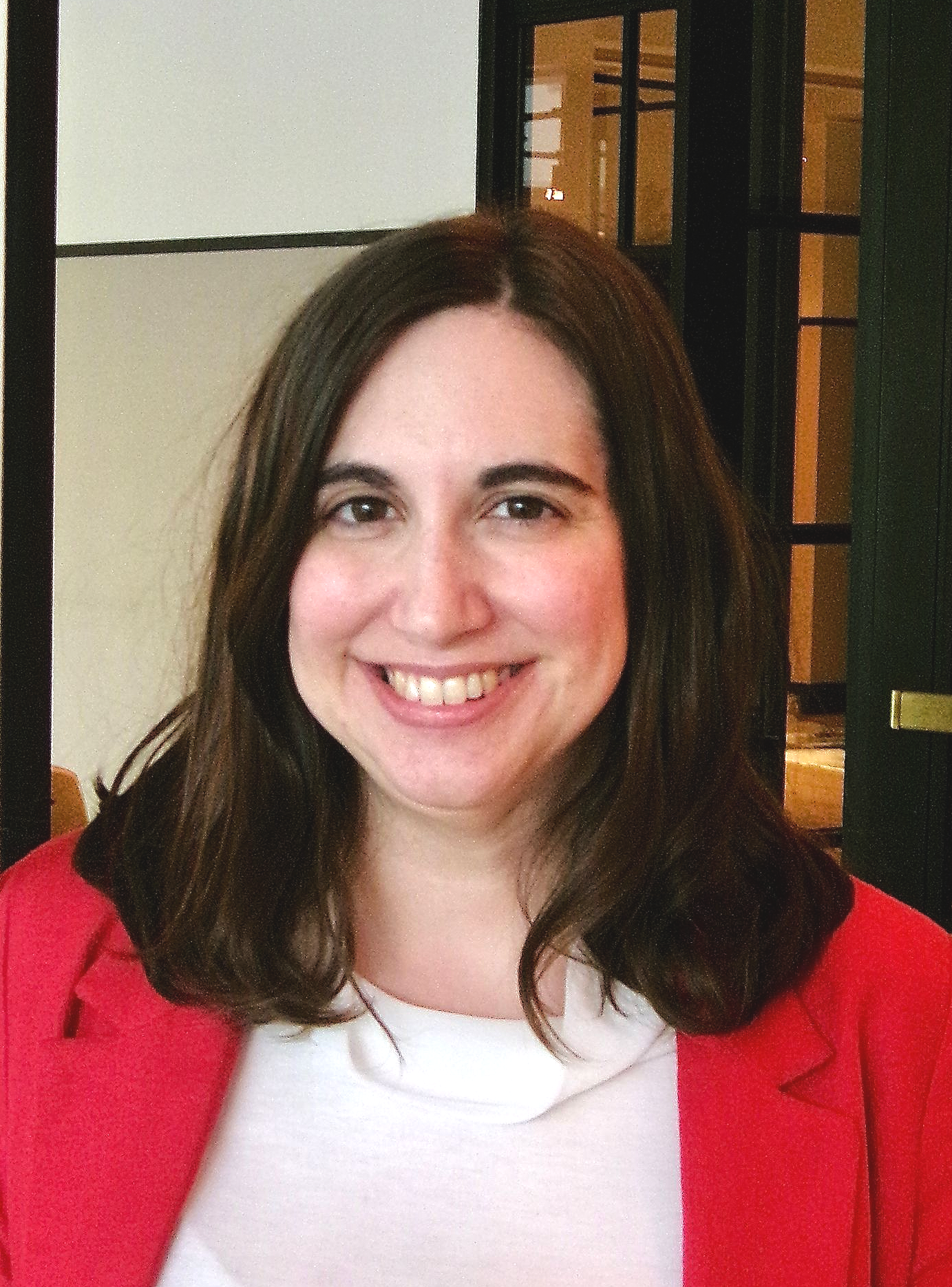 Brown haired woman in red blazer and white blouse smiles at camera.