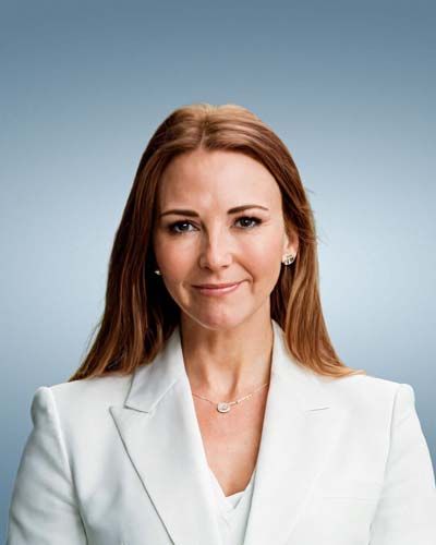 Woman in white blazer, long auburn hair, smiling, against a gradient blue background.