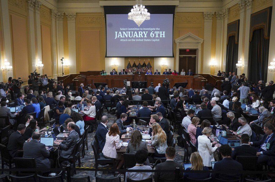 U.S. Capitol hearing room with people seated at tables, a panel at the front, and a screen showing