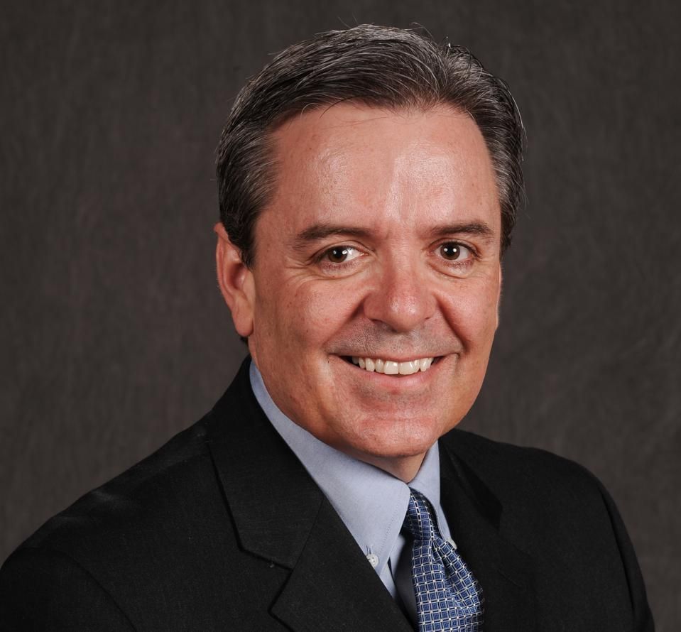 Man in suit smiles at the camera, against a dark gray background.