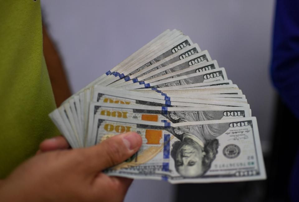 Hand holding a fanned stack of new $100 bills, bound with blue bands.