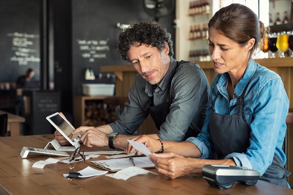 Two people at a counter reviewing paperwork and tablet, likely discussing finances in a cafe.