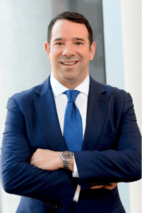 Man in blue suit, arms crossed, smiling.