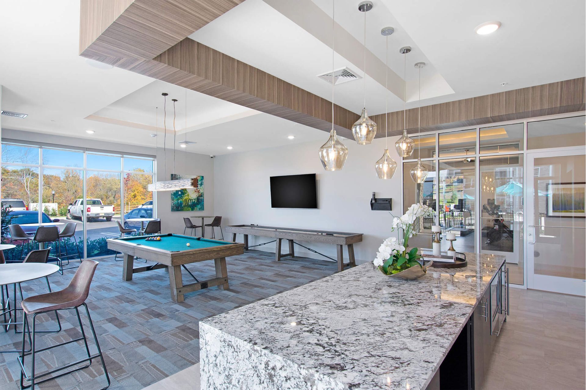 Modern community lounge with a pool table, granite island, pendant lighting, and glass entry doors at The Parc at Roxbury in  Roxbury, NJ.