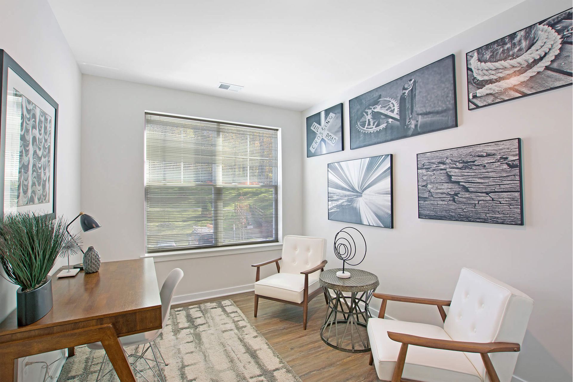 Small apartment office with a wooden desk, white chairs, a round metal table, and wall art at The Parc at Roxbury in  Roxbury, NJ.