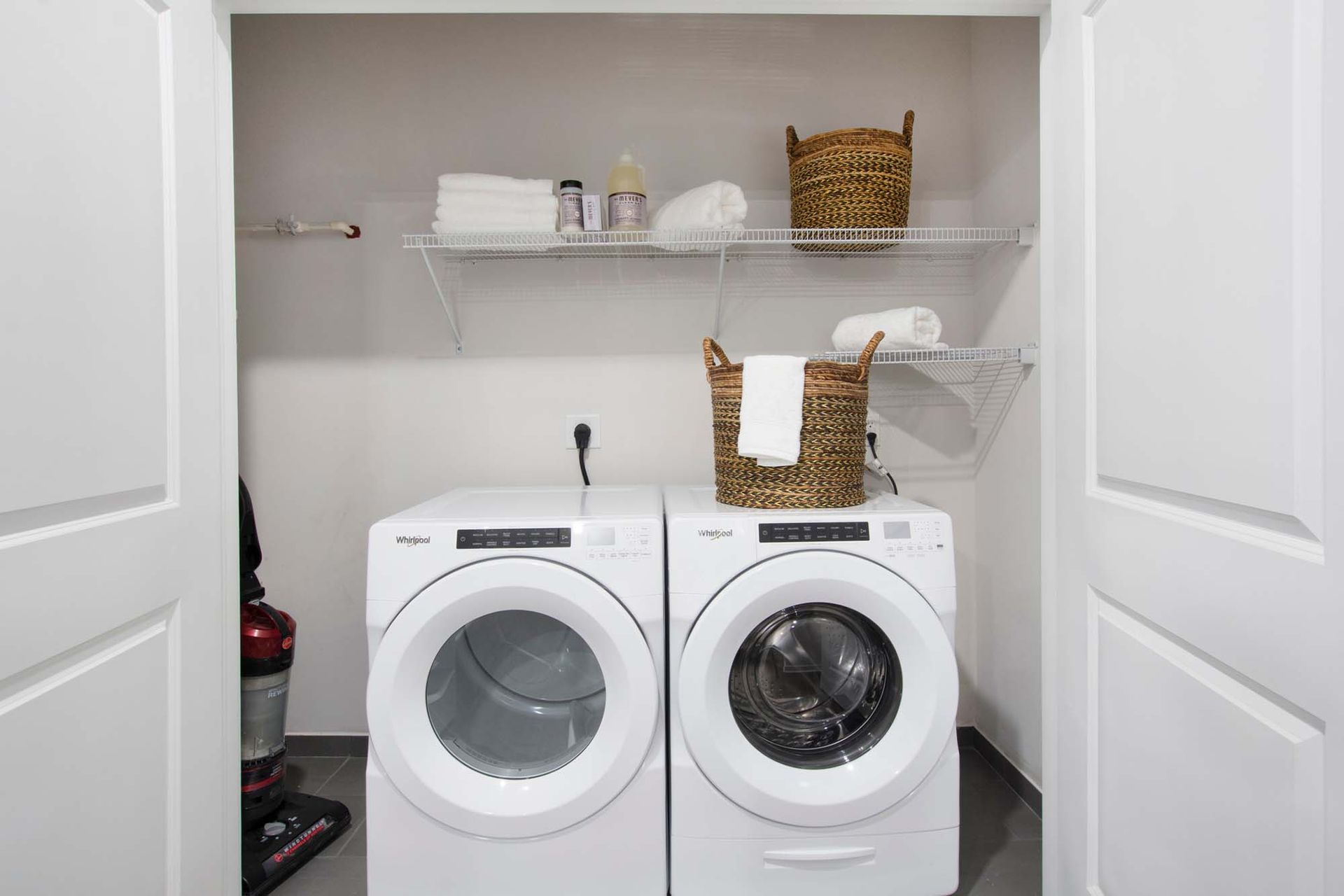 In-unit laundry closet with two front-loading washers and a dryer; white wire shelves hold towels and baskets at The Parc at Roxbury in  Roxbury, NJ.