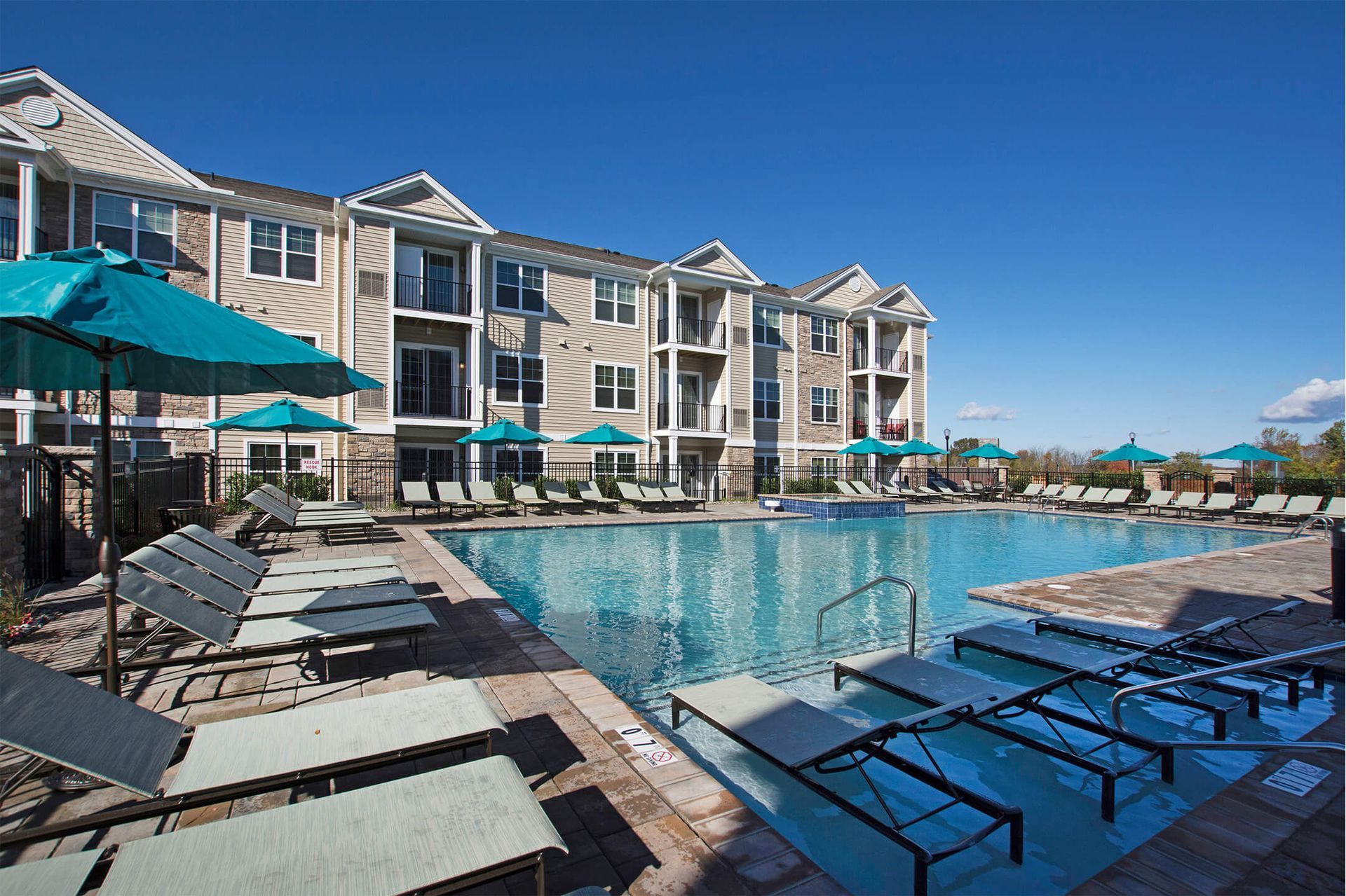 Outdoor pool area at an apartment community with teal umbrellas and lounge chairs at The Parc at Roxbury in  Roxbury, NJ.