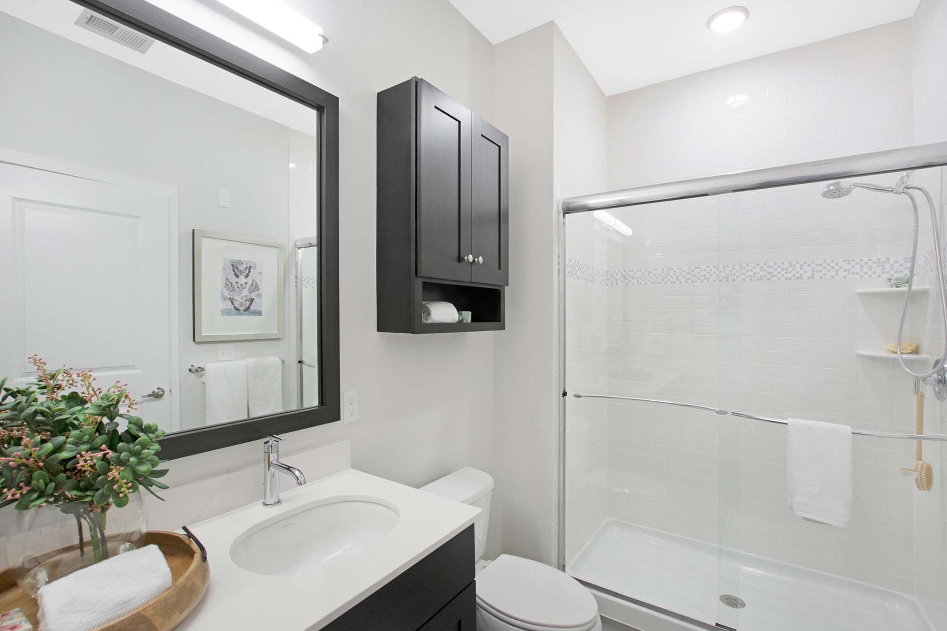 Modern apartment bathroom with white vanity, dark wall cabinet, and glass shower at The Parc at Roxbury in  Roxbury, NJ.