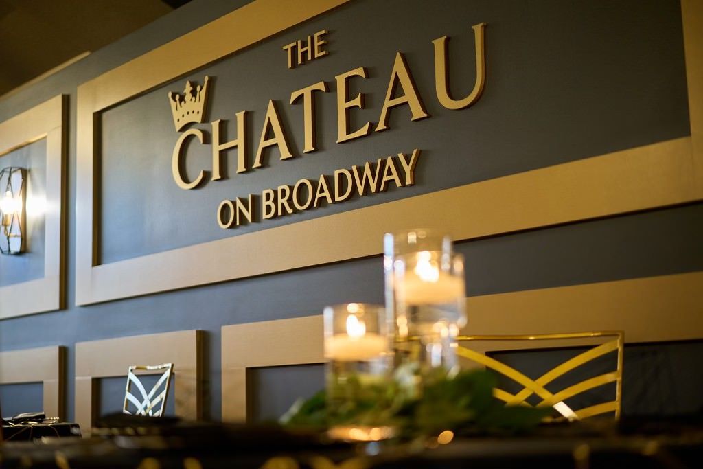 A sign for the chateau on broadway is on a wall next to a table with candles.