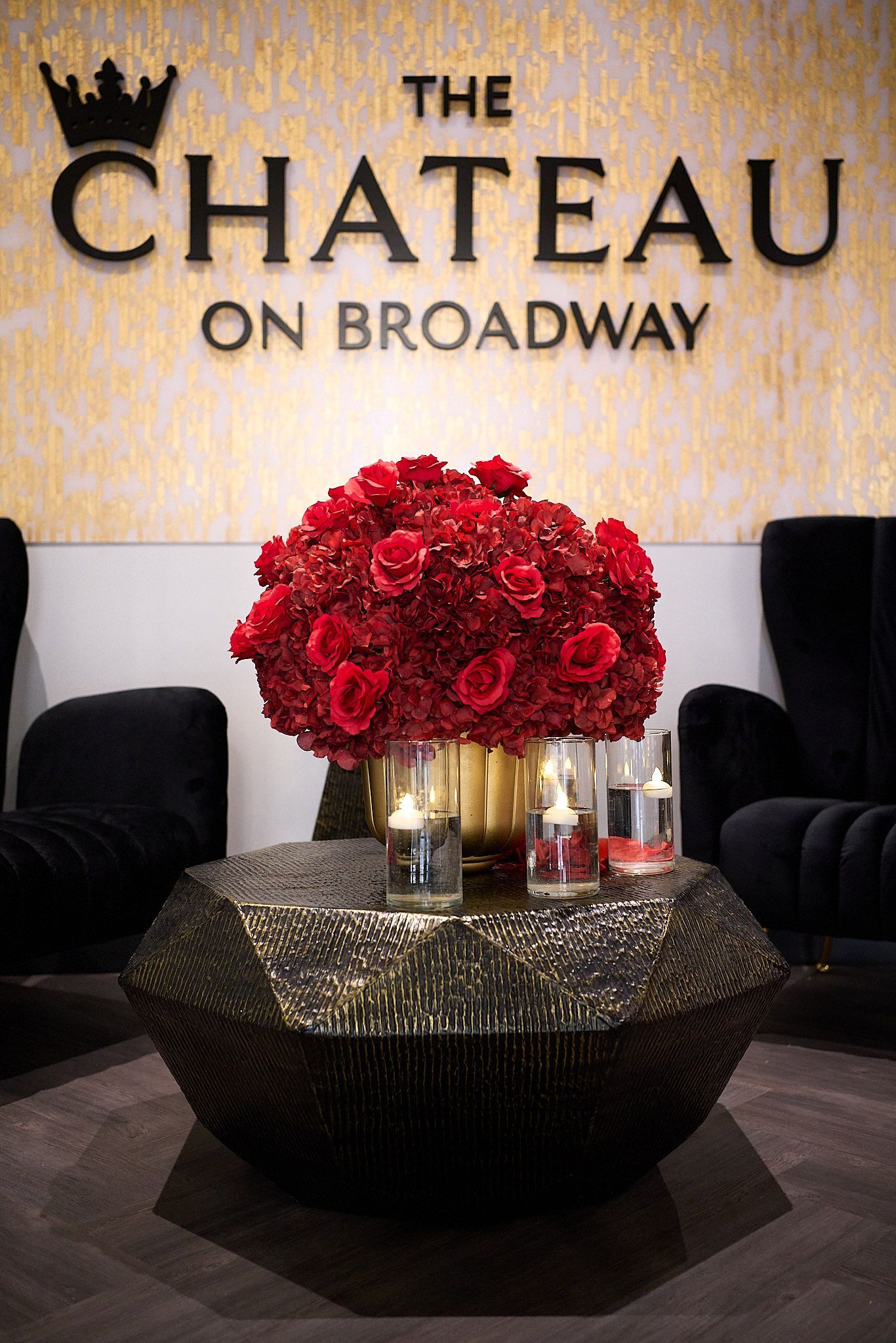 A table with a vase of red flowers in front of a sign that says the chateau on broadway
