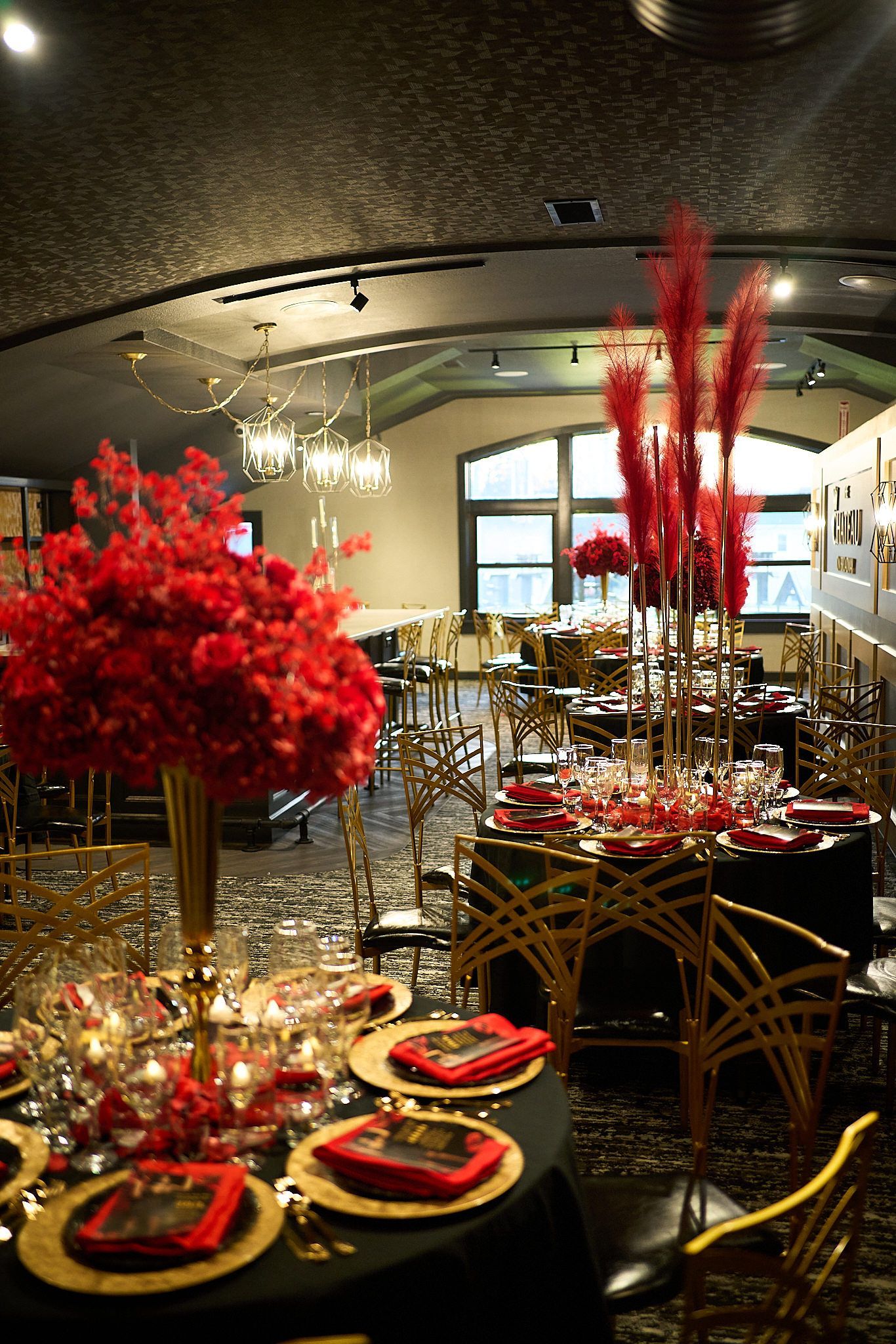 A large room with tables and chairs set up for a party with red flowers in vases.
