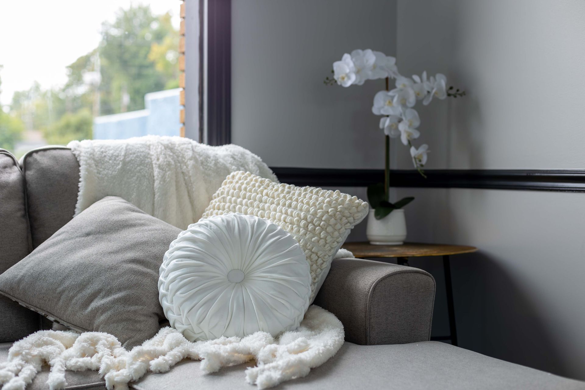 A couch with pillows and a blanket on it in a living room next to a window.