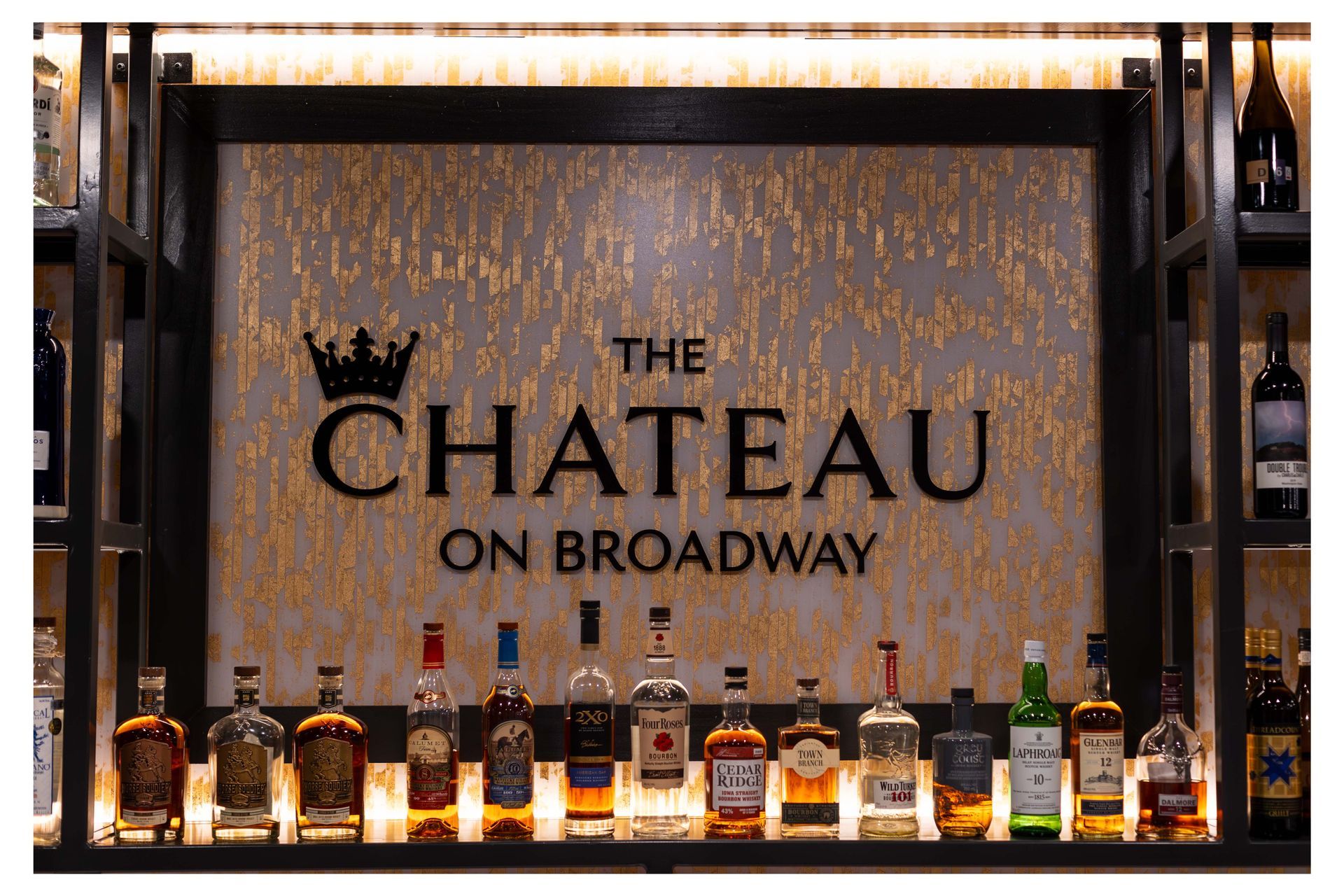 A sign for the chateau on broadway is above a shelf of liquor bottles.