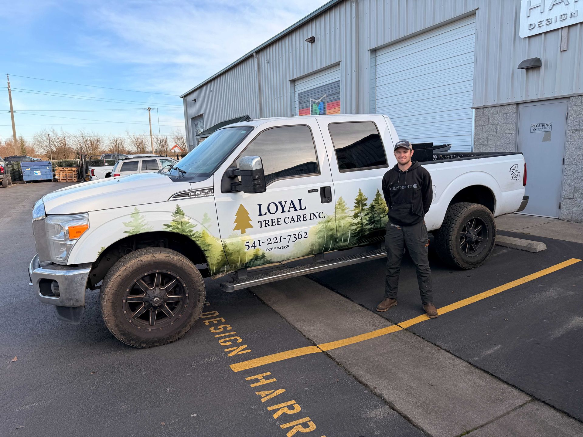 Man stands next to a white truck with business graphics in front of a building.