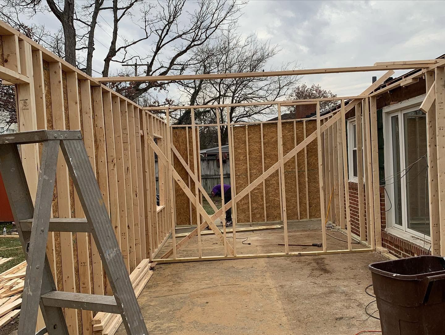 Partially framed outdoor corridor with wooden studs, ladder, and concrete floor under construction